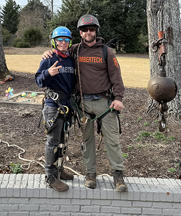 Two TimberTech crew members in helmets and climbing harnesses posing together in a residential yard